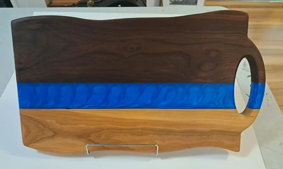 Walnut and cherry board with a blue resin river, on a stand